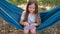 Child sitting in a hammock playing with pop it sensory toy. Girl presses on colorful rainbow squishy soft silicone