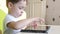 Child sitting at the table touches the touch screen of the tablet. A child is playing with a tablet and is smiling