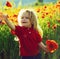 Child, smiling little boy in flower field of poppy with green stem on natural background. Summer fun for kids outdoors