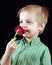 Child sniffing flower. boy with red rose on black