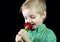 Child sniffing flower. boy with red rose on black