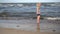 Child splashing sea waves with legs. Blond girl play with water on coastline