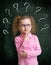 Child standing near school chalkboard with many question marks