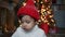 Child stands in front of a Christmas tree with toys near the fireplace