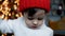 Child stands in front of a Christmas tree with toys near the fireplace