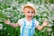 A child in a straw hat in daisy flowers in a field in summer at sunset. A blue-eyed and fair-haired disgruntled boy stands in a