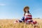 Child in straw hat holding american flag in golden field with wheat