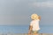 Child in a straw hat sitting on beach and looking at the distance. Holidays. Back view