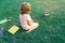 Child studies and learn outside. Little student having rest at school yard, reading book outdoors, sitting on lawn in