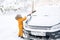 Child sweeps snow from the windshield of a car with a brush