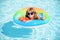 Child in swimming pool on inflatable ring. Little boy learning to swim with float. Water toy for toddler. Healthy