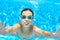 Child swims in pool underwater, funny happy girl in goggles has fun under water and makes bubbles, kid sport