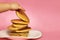 A child takes a pancake from a stack, pink background