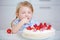 Child tastes of strawberry cake in kitchen