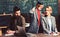 Child teach woman and man in school. Child in big suit coat and graduation cap together with family at desk, examination