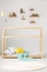 Child toys on shelves on a white wall and a wooden house bed frame for a toddler in a cute bedroom interior