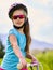 Child traveling bicycle in rainbow goggles and helmet in park.