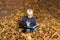 Child turns the pages in book. Boy sits in autumn forest and reading