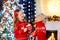 Child under Christmas tree at home. Little boy and girl in knitted sweater with Xmas ornament drink hot chocolate. Family with