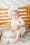 Child under one year old in a white cook apron and hat sits at a bench with baskets with rolls, bread, donuts, milk and flour