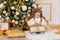 A child unwraps a new year`s gift near a Christmas tree with a gold decor at home
