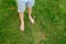 The child walks barefoot on the green grass. The concept of hardening, prevention of flat feet, meditation.