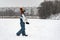 Child walks through snow-kept field. Boy in warm clothes plays outside in winter against the background of high-rise buildings