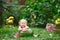 A child with a watermelon sits on the grass in a park with flowers.