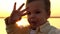 Child waving his hand in the camera against the backdrop of the setting sun