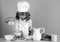 Child wearing cooker uniform and chef hat preparing vegetables on kitchen, studio portrait. Cooking, culinary and kids