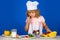 Child wearing cooker uniform and chef hat preparing vegetables on kitchen, studio portrait. Cooking, culinary and kids