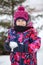 Child wearing warm clothes as puffer jacket and mittens walking at winter day, holding snowball