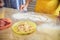 Child wearing yellow apron, playing with flour on table. Close-up picture of hands, drawing shapes on flour. Bakery master class