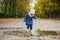 Child wearing yellow rain boots and jumping in puddle