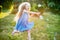 Child whirling, dancing plays on the meadow. Girl having fun with bubbles. Cute little longhair blonde girl dancing with soap
