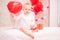 Child with white feather wings holds a red balloon in the shape of a heart, the symbols of Valentine`s Day