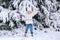 Child in white warm winter clothes and knit hat looking at the falling snow In winter forest