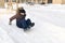 A child in winter clothes, cheerfully rolls down from a snow slide with wooden railings and stairs, in winter