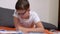 Child Writing with a Pen in a Notebook, Lying on an Orange Bedspread in the Room