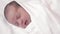 Childhood, infancy, parenthood, motherhood concept - close-up portrait of a newborn baby lying on a white beige bed