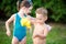 Childhood summer games with water pool. Caucasian brother and sister play with plastic toys watering can pouring water splashing,