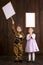 Children boy are dressed as soldier in retro military uniforms and girl in pink dress. They`re holding blank posters for veterans