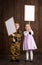 Children boy are dressed as soldier in retro military uniforms and girl in pink dress. They`re holding blank posters for veterans