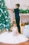 Children, a boy and a girl in a white ball gown near a Christmas tree in holiday dresses with gifts and silver confetti.