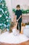 Children, a boy and a girl in a white ball gown near a Christmas tree in holiday dresses with gifts and silver confetti.