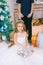 Children, a boy and a girl in a white ball gown near a Christmas tree in holiday dresses with gifts and silver confetti.