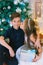 Children, a boy and a girl in a white ball gown near a Christmas tree in holiday dresses with gifts and silver confetti.