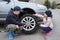 Children at the broken car, looking at the wheel.  Car repair services