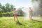 Children brother and sister, playing with watering hose in hot summer afternoon