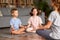 Children brother and sister sitting in lotus pose on floor and meditating with closed eyes with mom